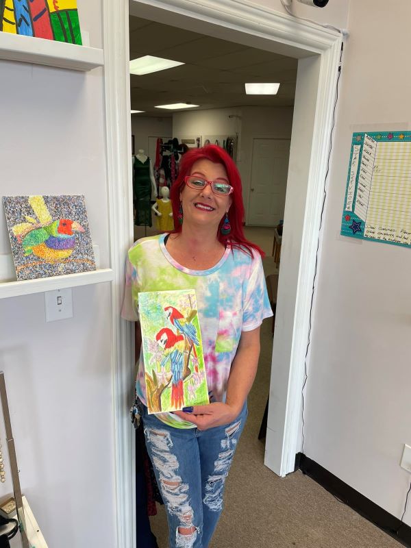 A woman holding a painting of two parrots